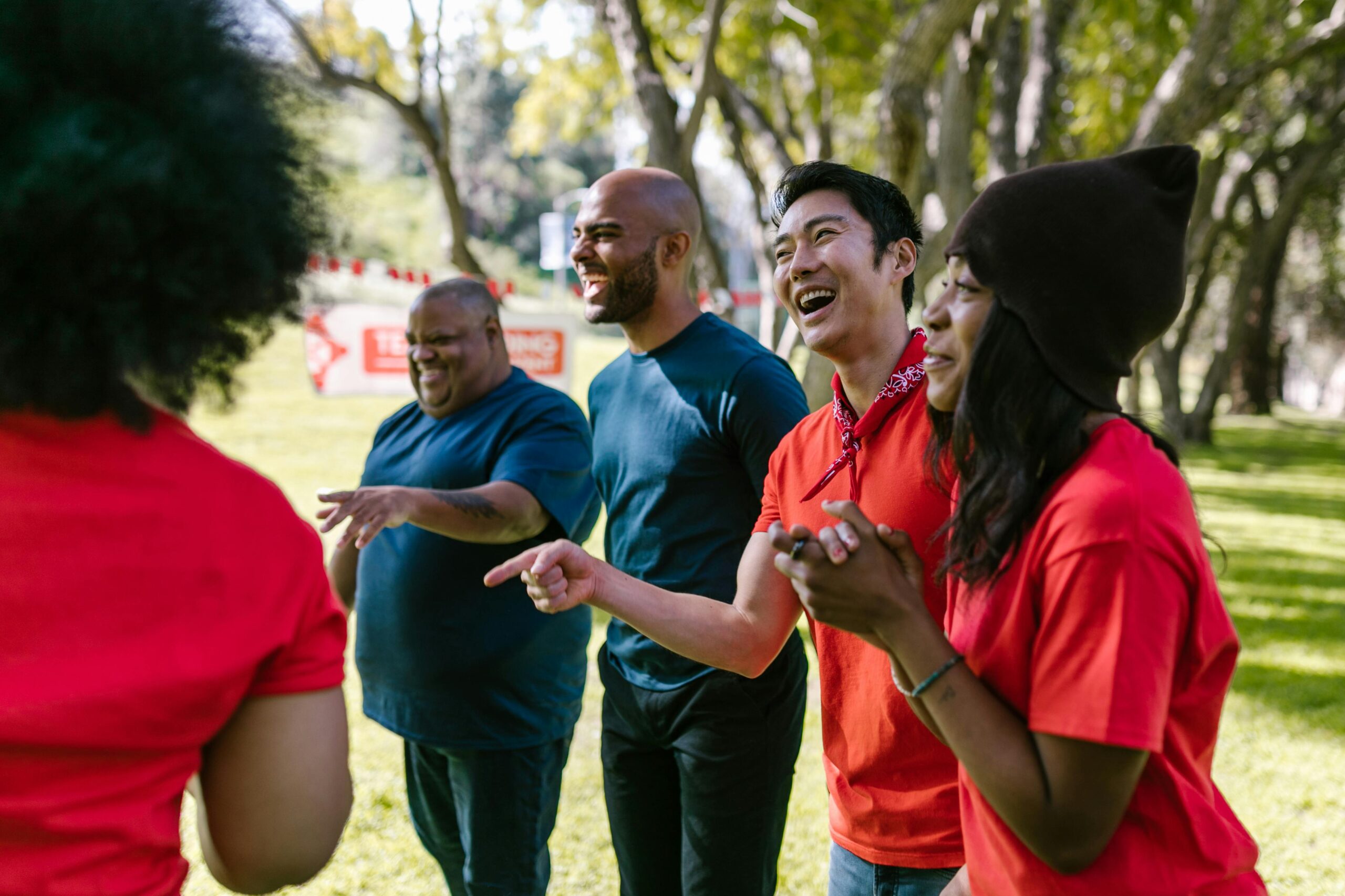 A group of four adults standing outdoors in a park, laughing and smiling together on a sunny day.