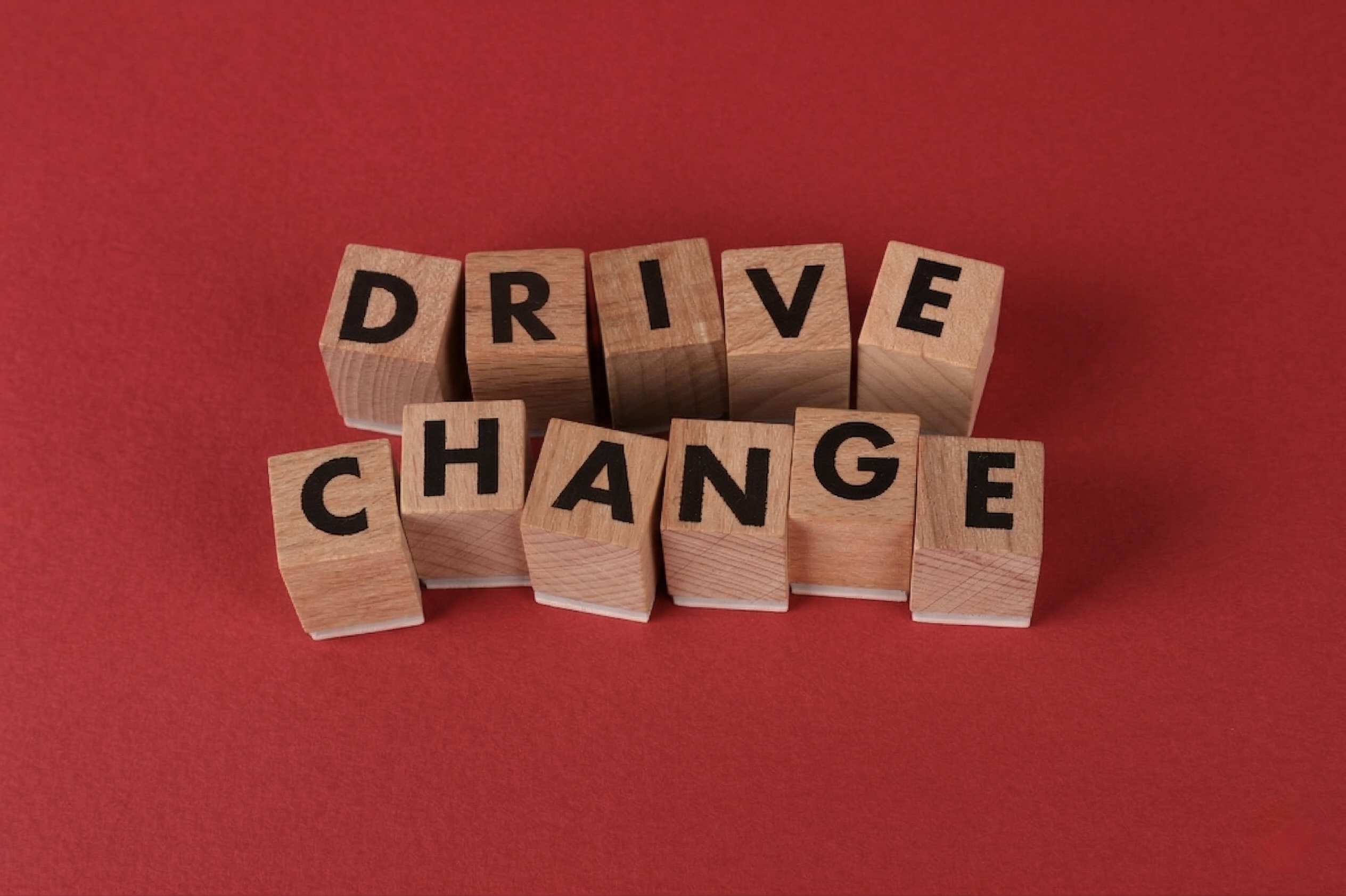 Wooden letter blocks spell "DRIVE CHANGE" on a red background. The words convey motivation and action in a bold, impactful way.