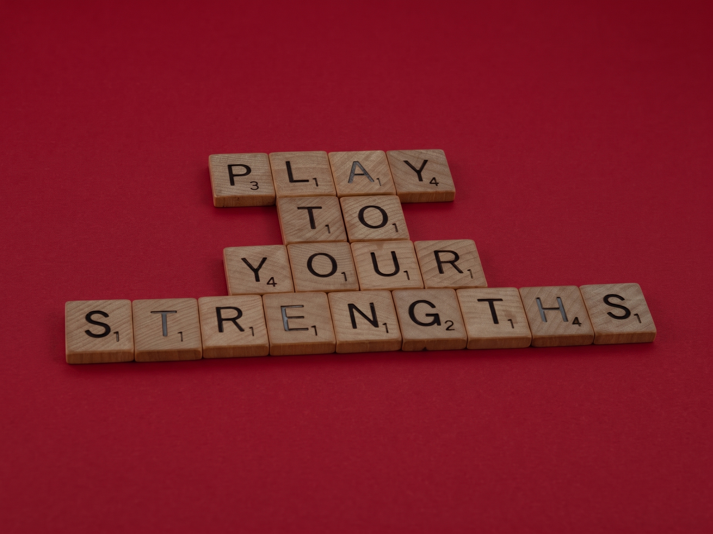 A picture of scrabble pieces on a dark red background that read 'Play to your strengths'